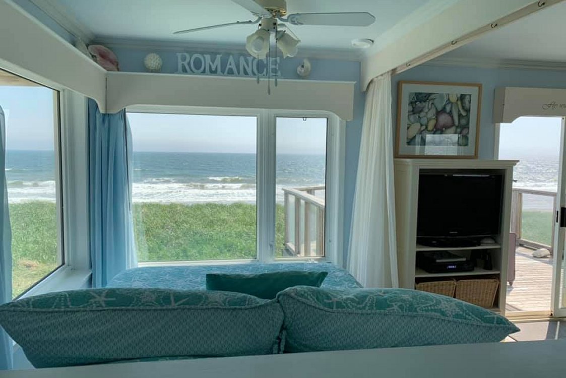 View of the beach, sand and grass from the queen bed. Watch sunrises over the ocean, and hear the ocean in Sea Spray Suite bedroom.